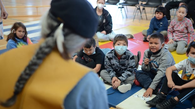 A young boy asks a question of an older man with a long grey braid. 