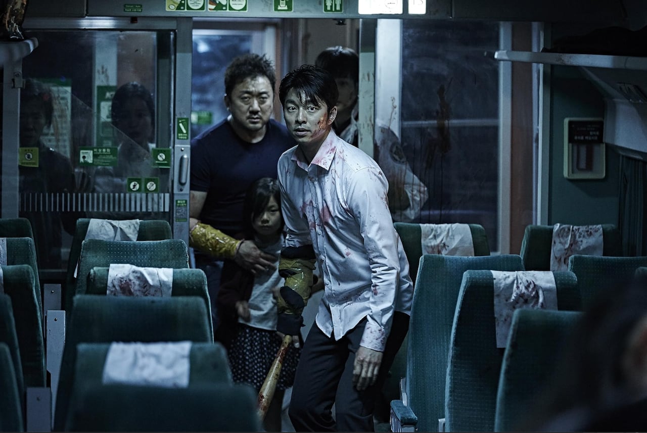 People standing on a train with blood on them. One man is holding a baseball bat.