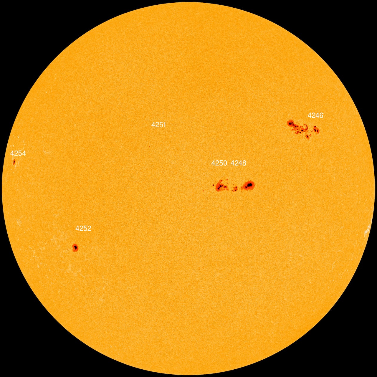 The Sun's orange disk is dotted with several dark regions.