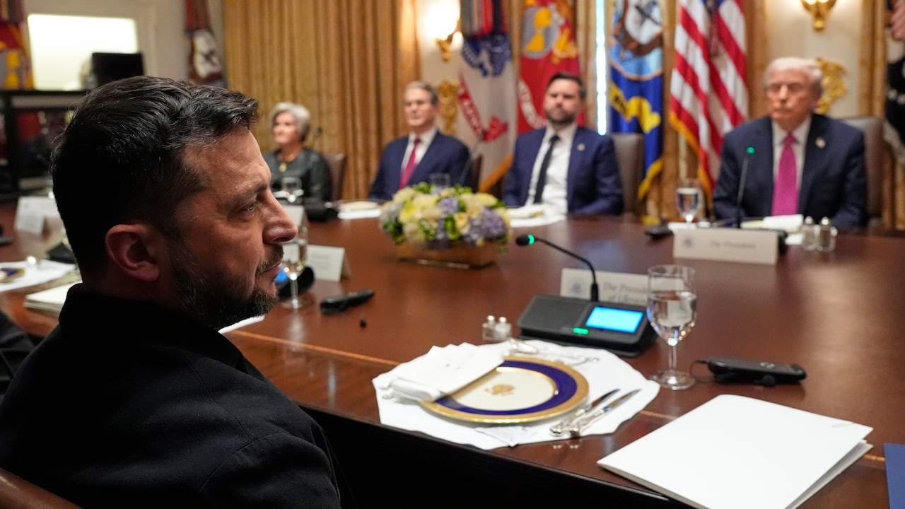 Zelenskyy is seen in profile in the foreground, with Trump, Vice President JD Vance, Treasury Secretary Scott Bessent and White House Chief of Staff Susie Wiles visible in the background across a table.