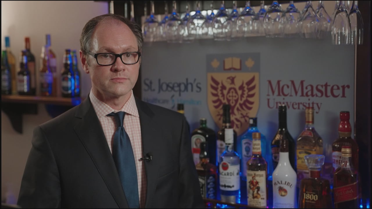 Vīrietis stāv pie alkohola pudelēm un uzraksta “Makmāstera universitāte” un “St Joseph's Healthcare”.