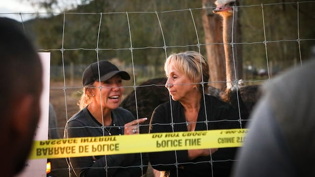 Karen Espersen, right, the co-owner of Universal Ostrich Farms, speaks with supporters with her daughter, Katie Pasitney, at the farm in Edgewood, B.C., on Monday, Sept. 22, 2025, as the Canadian Food Agency prepares to cull 400 of the farm’s ostriches this week. Two women stand behind a wired pen fence.