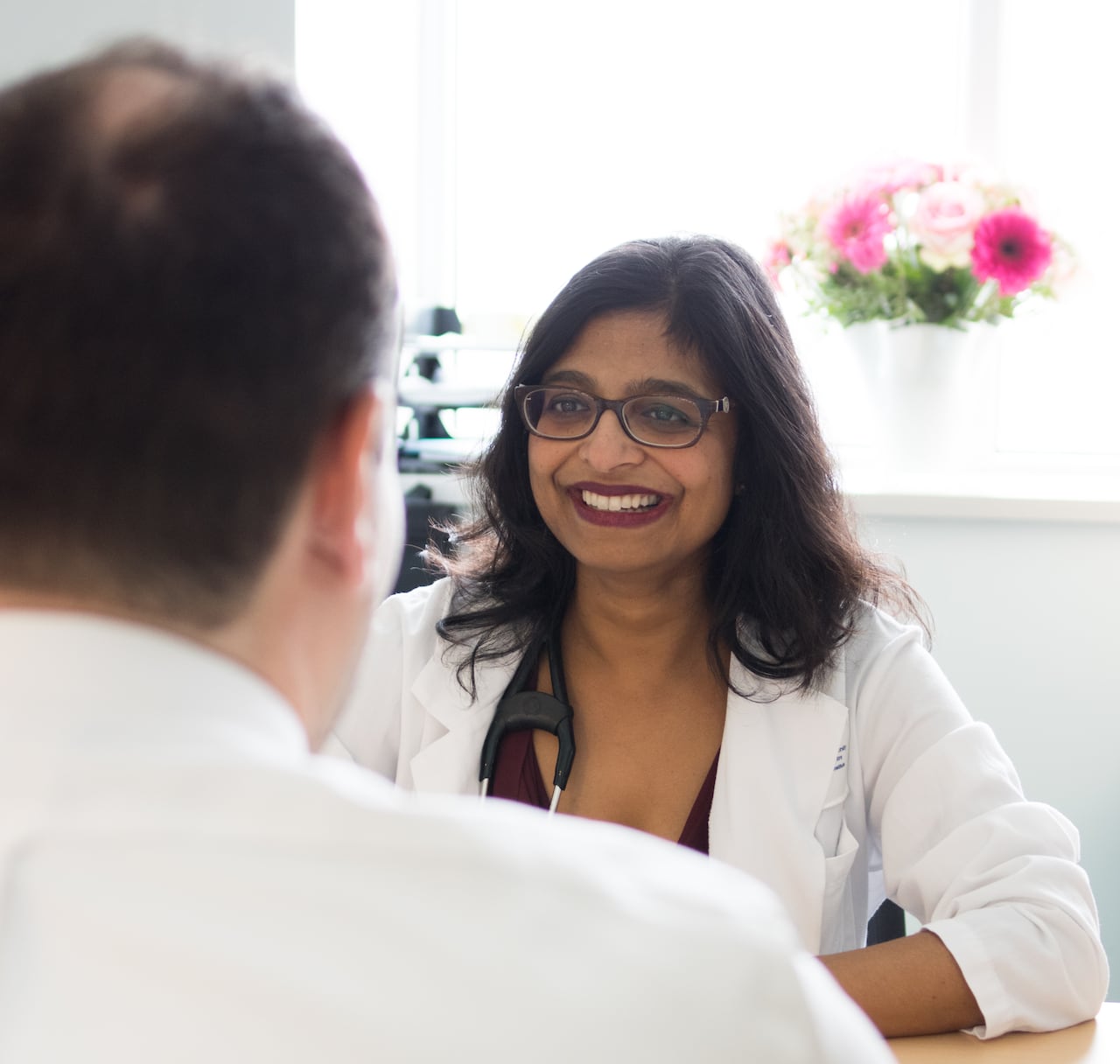 A physician in a white coat speaks to a man in her office.