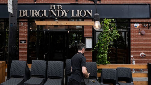 Adam Fazackerley, an employee at Pub Burgundy Lion opens the patio in Montreal, the pub's exterior sign is visible.