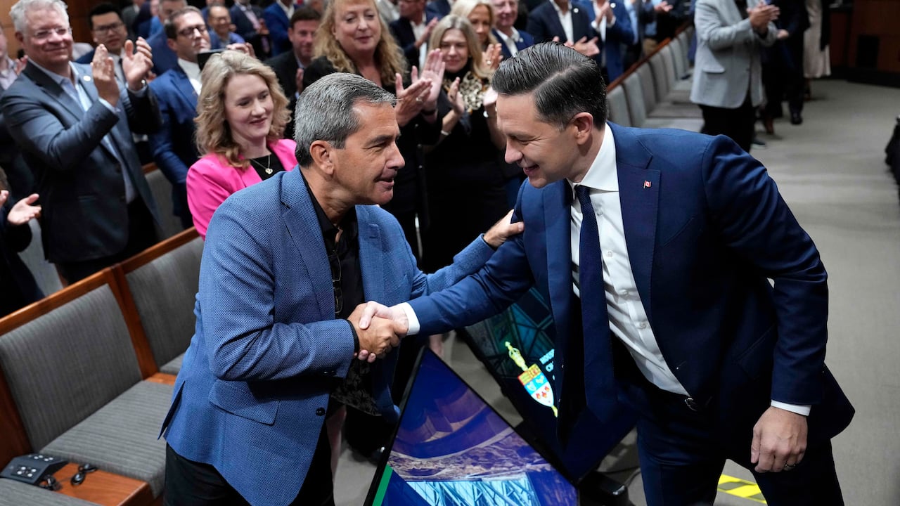 Two men in blue suits shake hands as a crowd applauds.