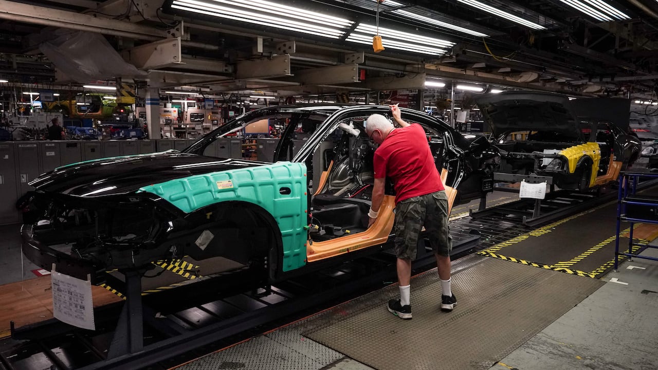 An auto worker leans into a partly made car An auto worker leans into a partly made car
