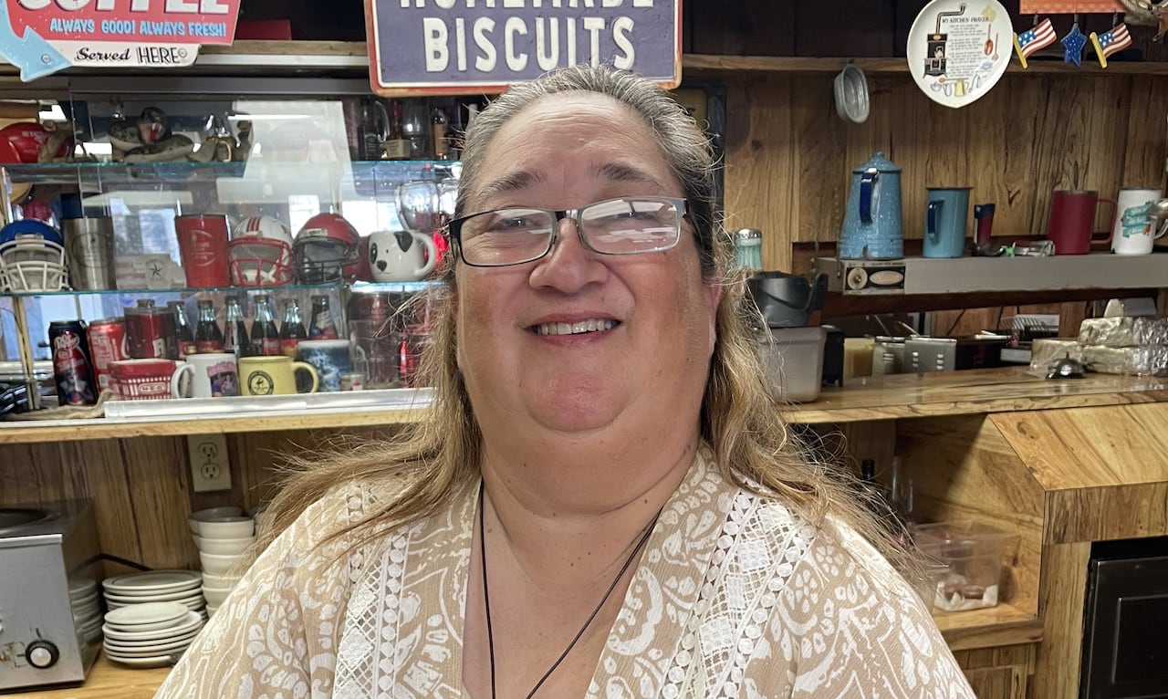 A woman stands smiling at the restaurant counter.