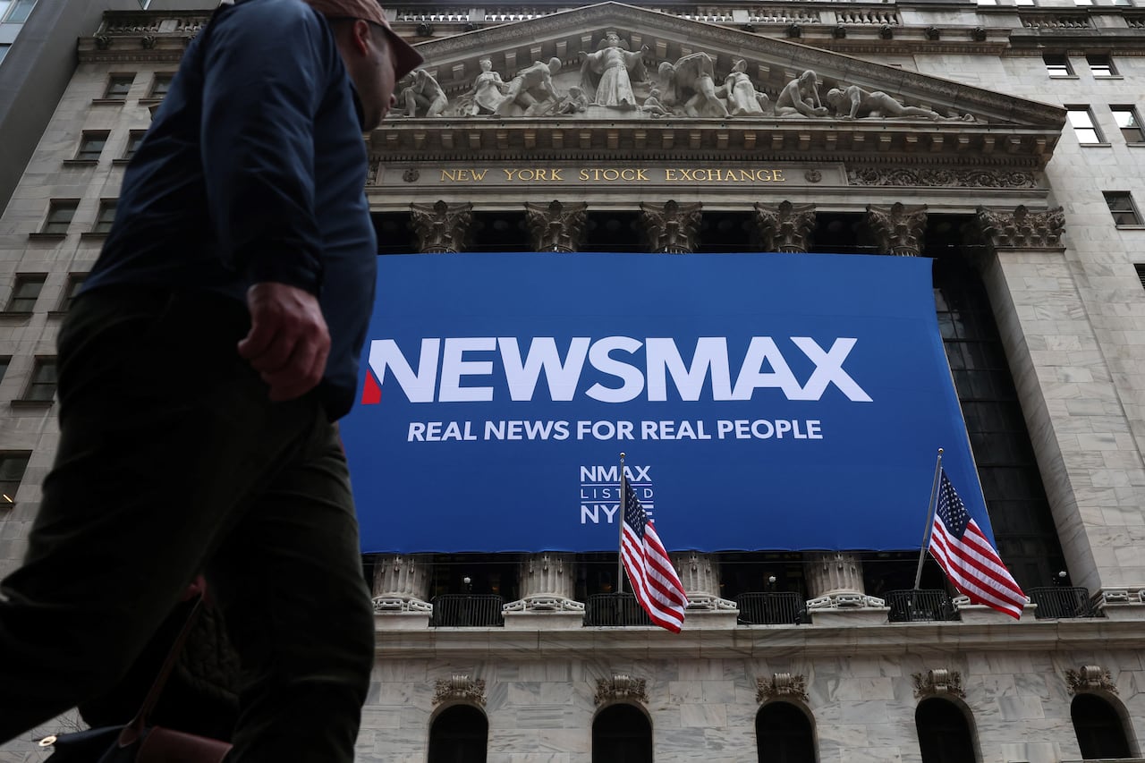 Exterior of the New York Stock Exchange, a plane sign reading Newsmax