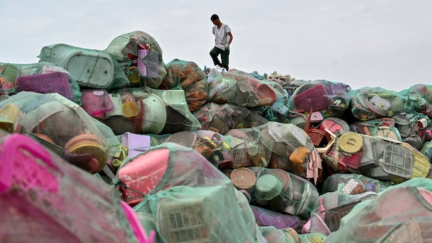 The person stands on top of a pile of bags that contain plastic products that have been ignored