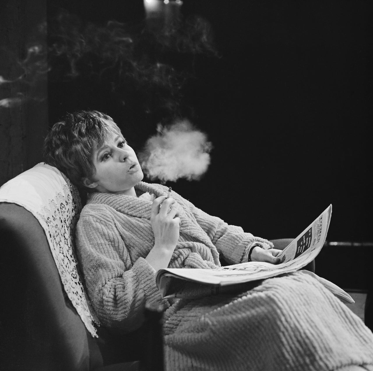 一張舊的黑白照片顯示，一名婦女坐著，靠在椅背上抽煙。 