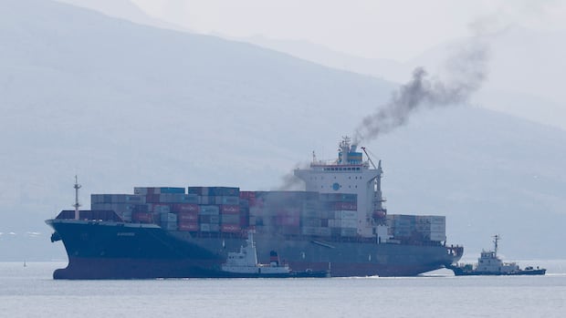FILE - Cargo ship M/V Bavaria is assisted by tug boats as it prepares to dock at Subic port in Zambales province, northwestern Philippines on Thursday, May 30, 2019. The head of the United Nations called Monday for maritime nations to agree on a course for the shipping industry to reduce its climate-harming emissions to net zero by the middle of the century at the latest. Cargo ship and tugboat spew fumes