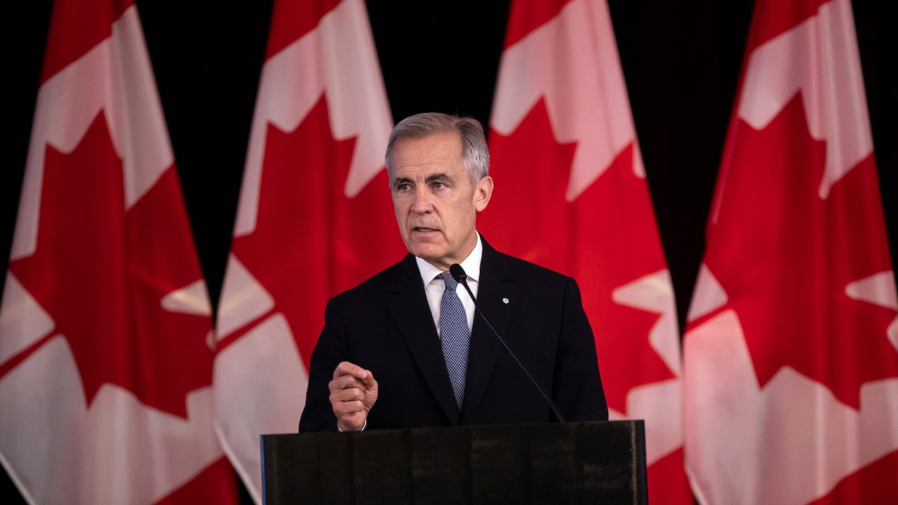 Man in suit at lectern in front of Canadian flags
