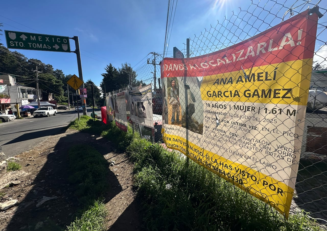 A banner hangs from a chain link fench by a narrow road.