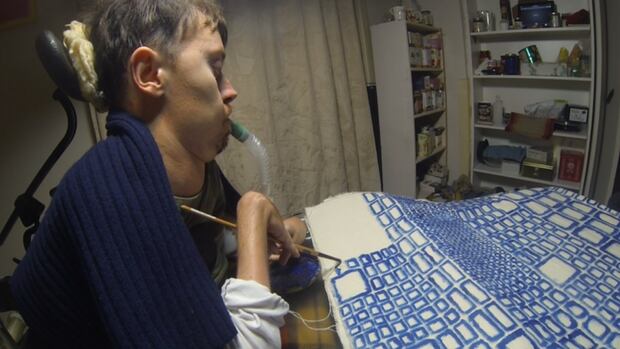 Ottawa artist Chris Binkowski, a.k.a. Bucko, posts videos of making his art. A man seated at a table paints a series of blue rectangles on white canvas.