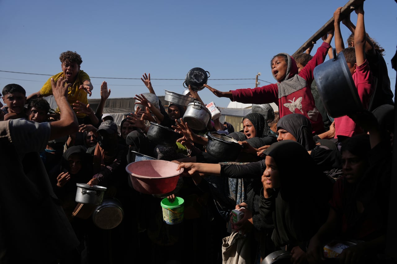 People hold pots and pans together and reach for food at the distribution point.