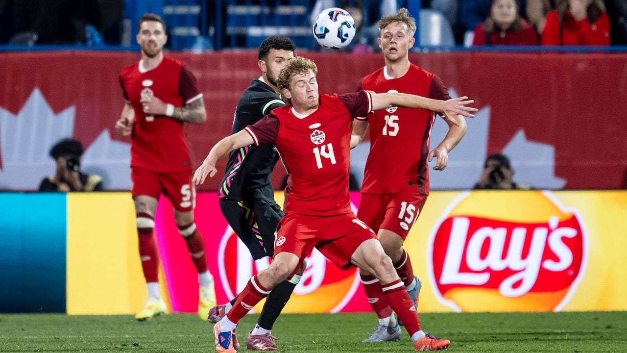 Two opposing soccer players tussle for the ball during a match.