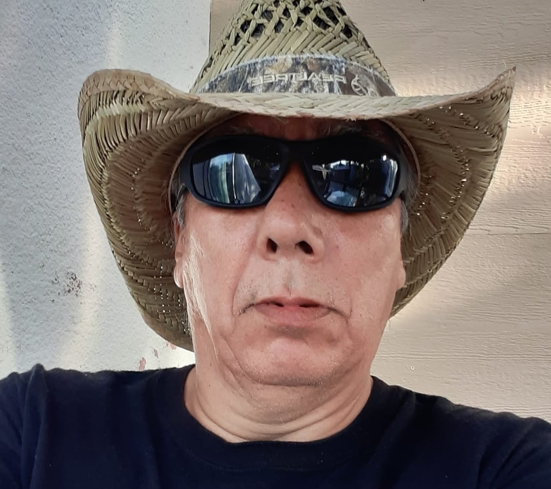 A man in a straw cowboy hat and sunglasses wearing a black tee shirt in a selfie photo