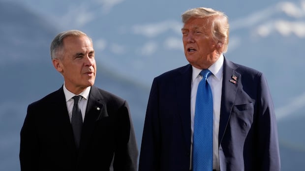 Two men in suits stand side by side. There are mountains in the background.