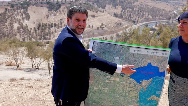 Man in suit gestures toward poster sized map he is holding.