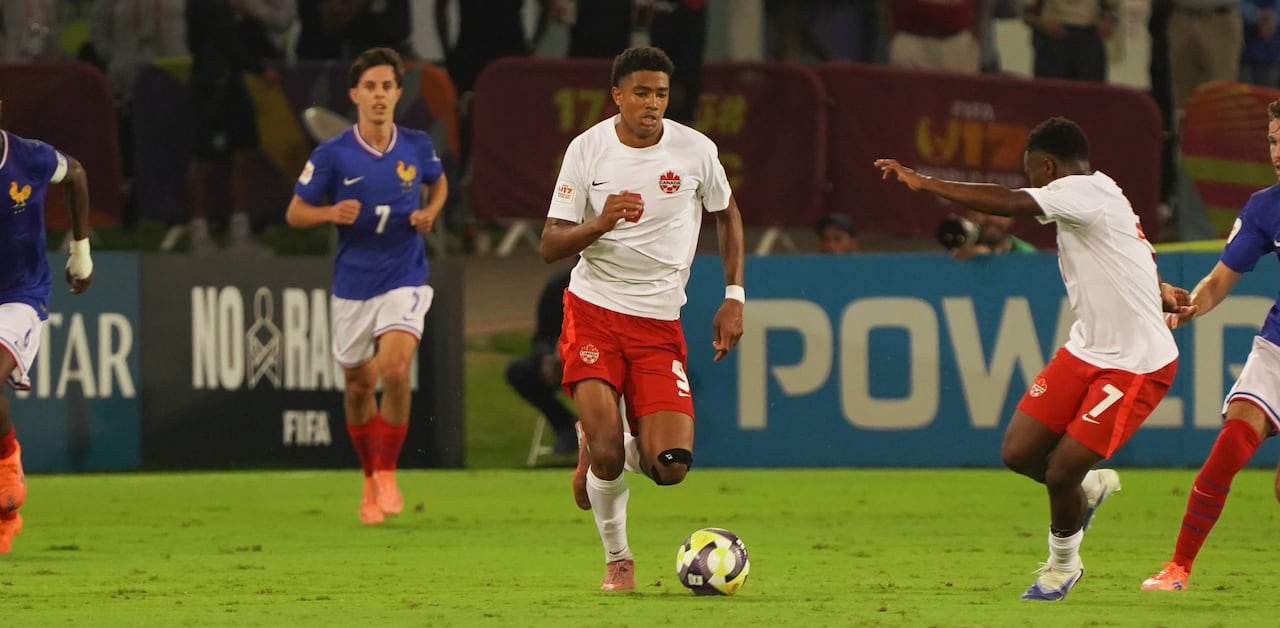 A soccer player representing Canada dribbles the ball.