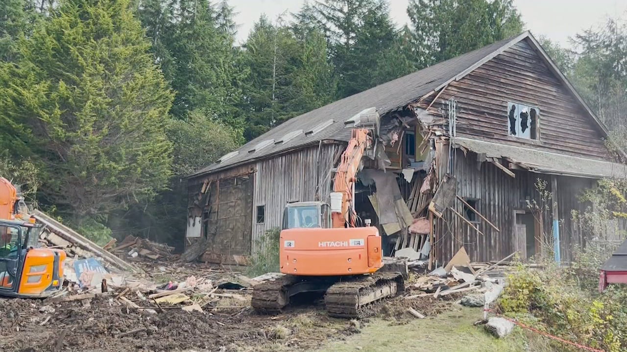 An excavator tears into a wooden building.