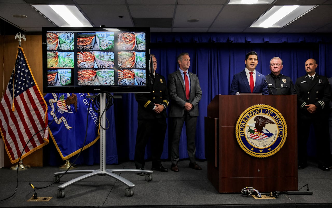 Law enforcement officials speak at a podium with a TV monitor next to them.