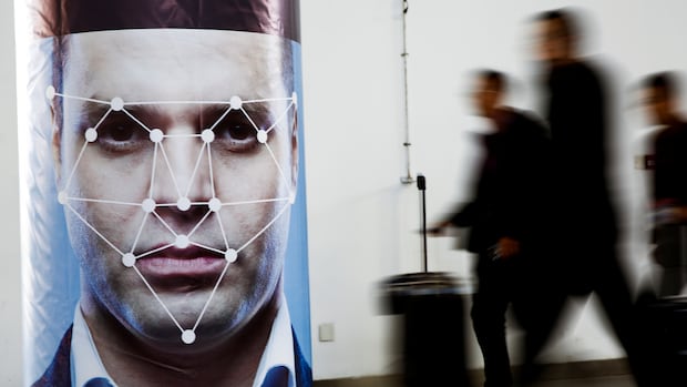 The United States is expanding its facial biometrics program with the goal of collecting images of non-U.S. citiznes at entry and exit points at all airports, seaports and the land border. People walk past a poster simulating facial recognition software.