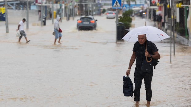 People walk along a flooded street in Ibiza on September 30, 2025. (Photo by Vicent MARI / AFP) (Photo by VICENT MARI/AFP via Getty Images) A man walks through water with an umbrella