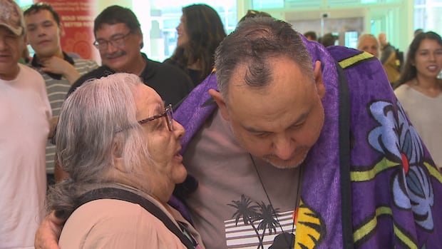 Jonathan Hooker was adopted by a New Zealand couple as part of the Sixties Scoop in 1975. He arrived back in Manitoba on Wednesday. A man with a blaknet around him with his arm around an older woman.