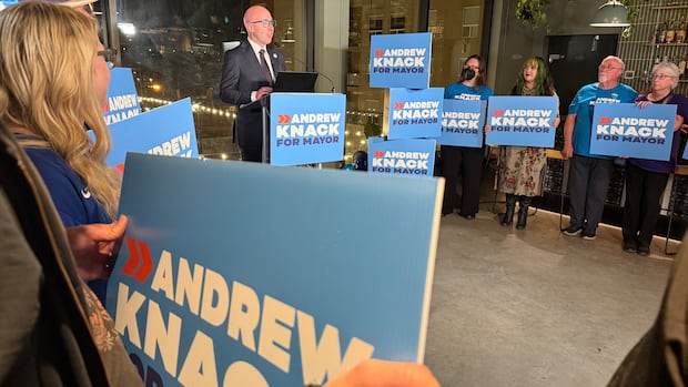 Andrew Knack at a podium speaking. Supporters are around him in a circle. 