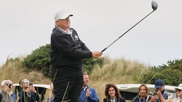 An older man with a white ball cap swings a golf club as a crowd looks on.