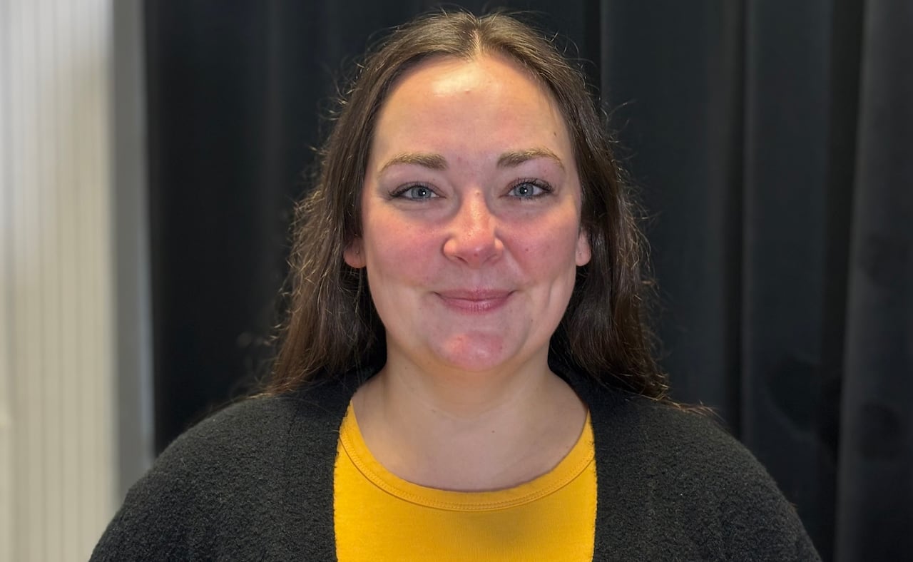 A grinning pistillate   with agelong  brownish  hair, wearing a yellowish  garment  and achromatic  cardigan.