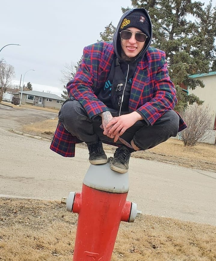 A young man in a hood and holding a butterfly knife squats on top of a fire hydrant in Dawson Creek