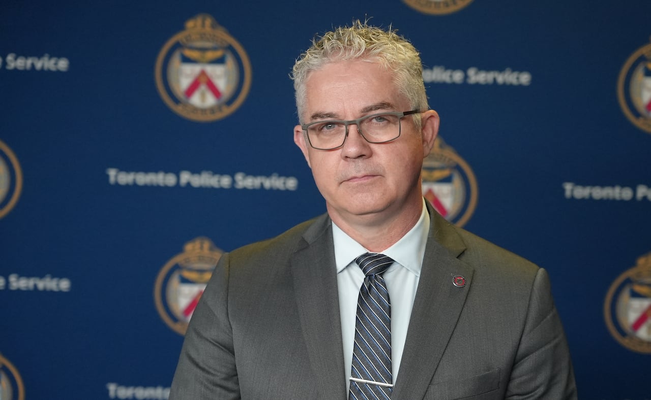 Man in a suit standing in front of a wall with Toronto police logos on it.