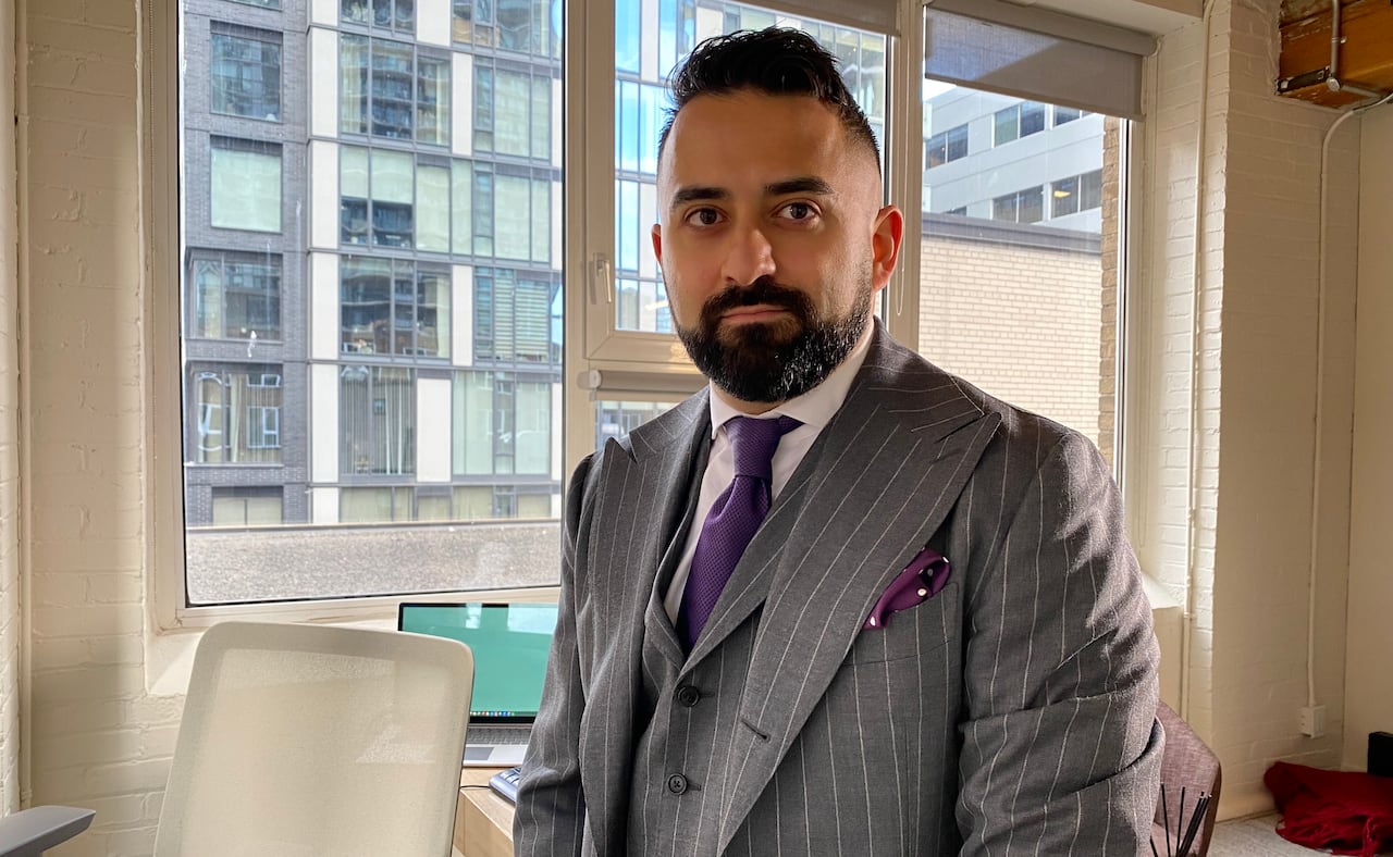 Justin Nasseri, dressed in a gray suit and purple tie, stands at his desk with a window behind him.