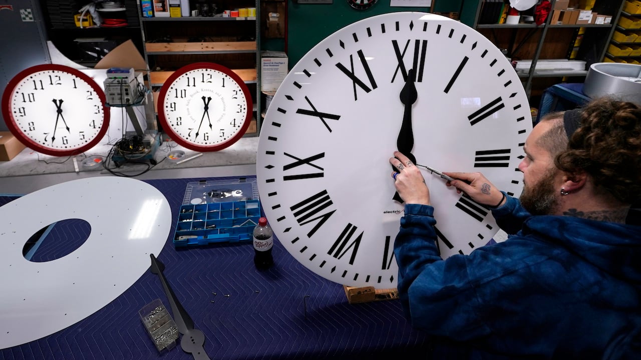 A antheral uses a instrumentality to set the hands of a ample analog clock.