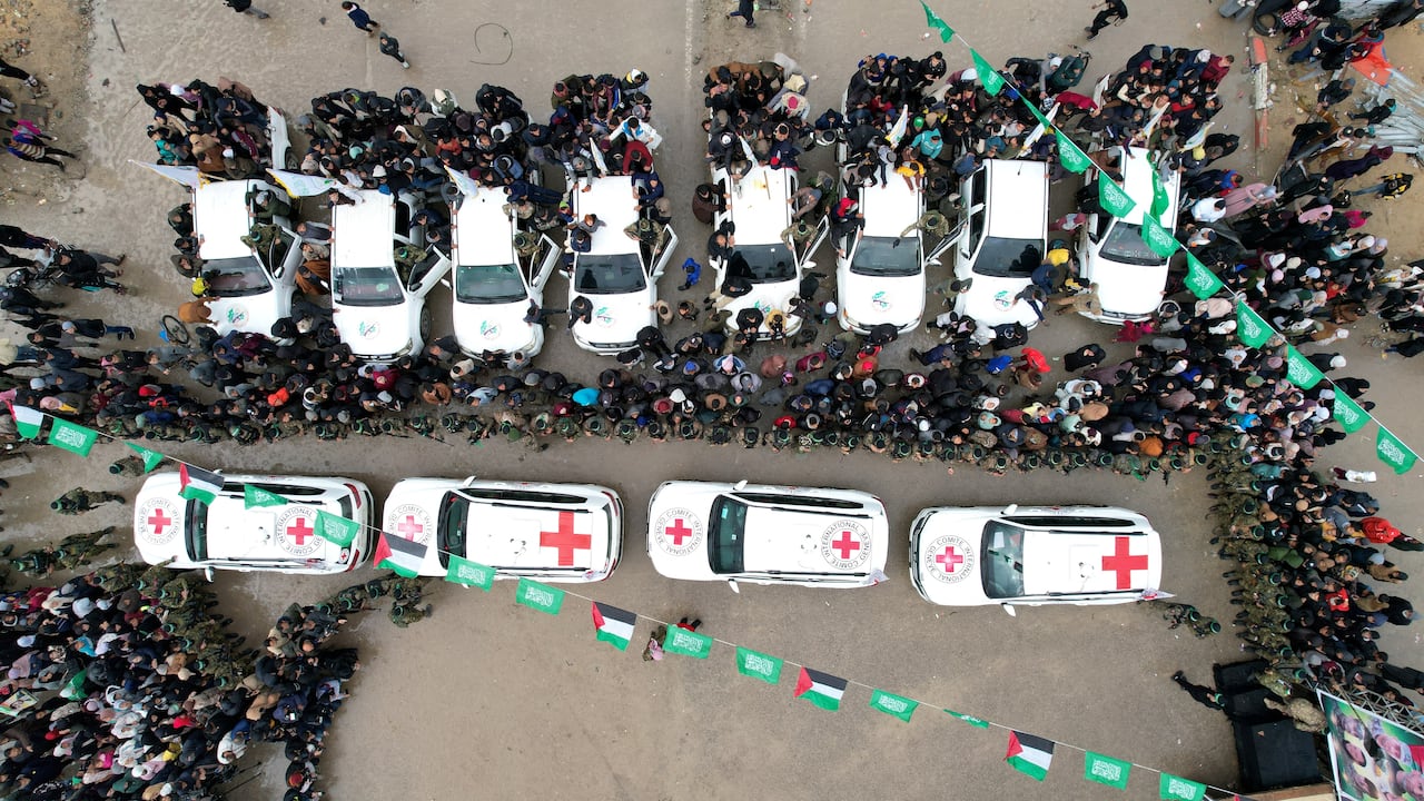 The photo taken from above shows a line of white vehicles with red crosses driving through a crowd of people