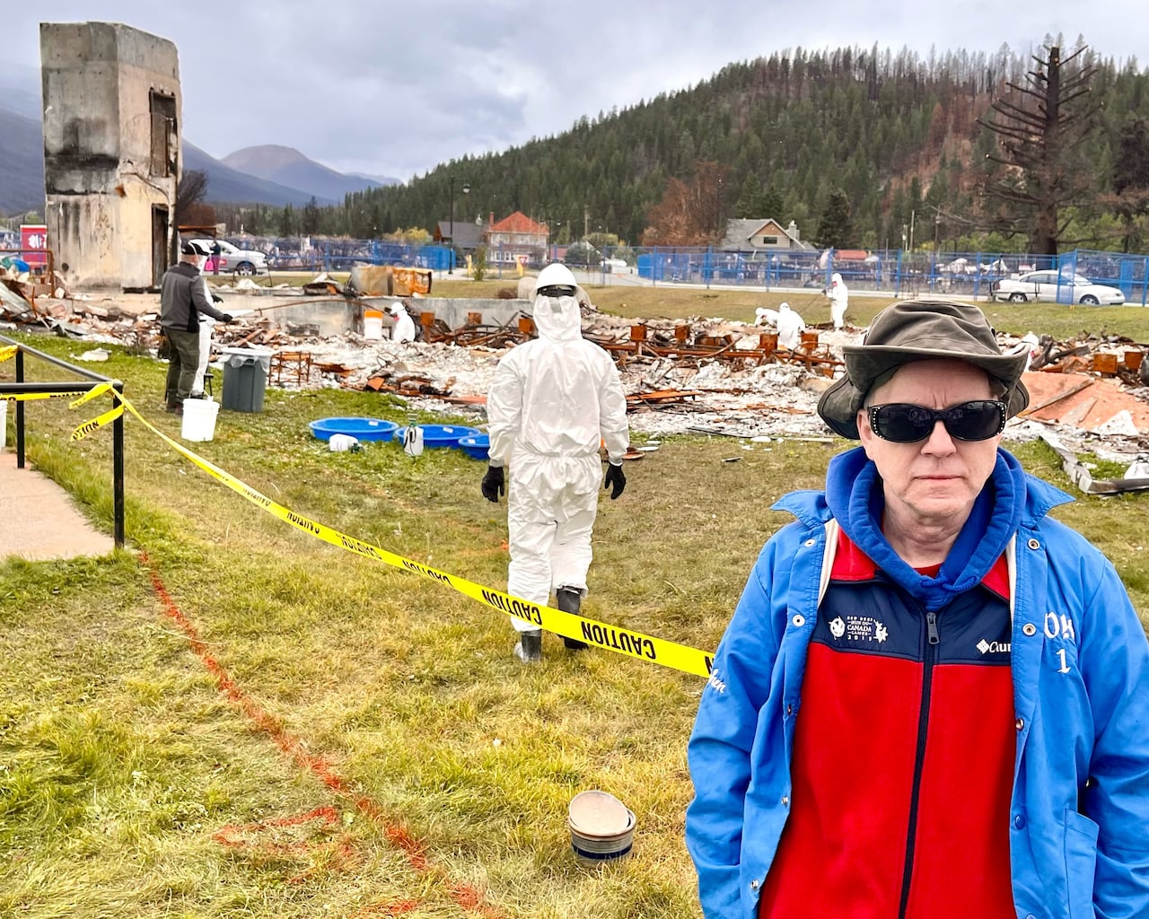 A antheral   successful  reddish  and bluish  covering  with sunglasses connected  stands earlier  the tract  of a burnt operation   portion    telephone  successful  hazmat suits cleanable  the wreckage.