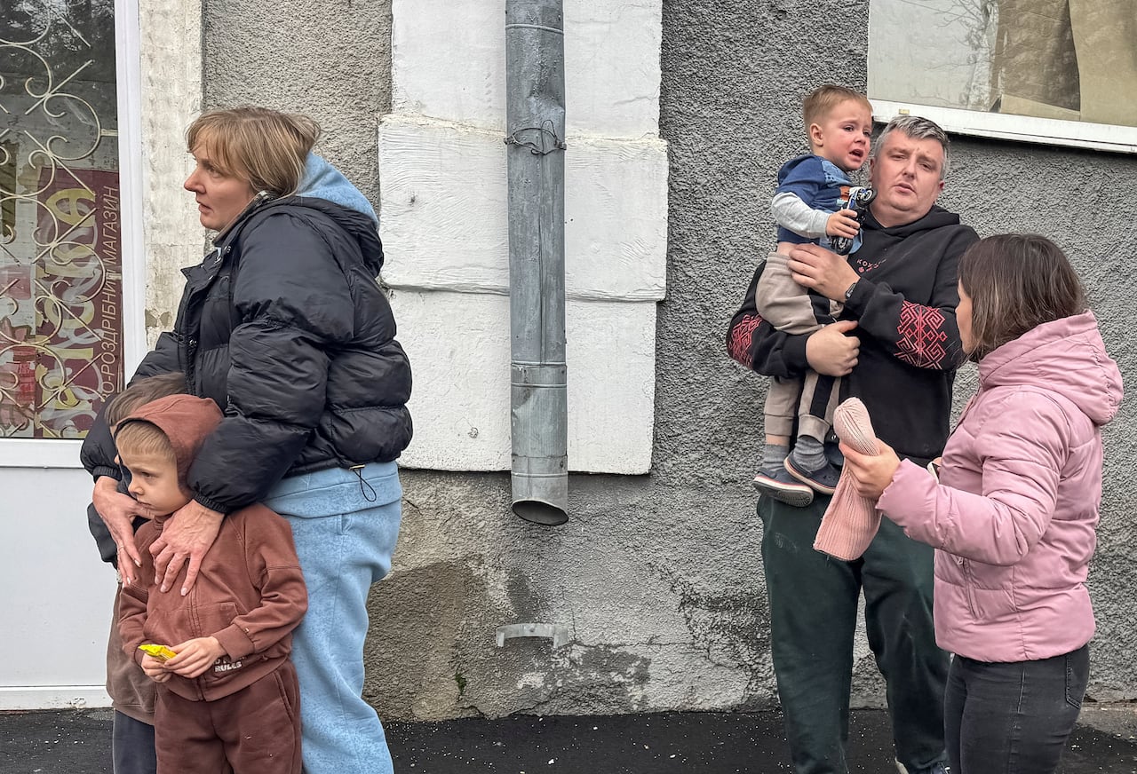 A man and a woman are shown with children, including a boy resting on the man's shoulder, in an outdoor photo.