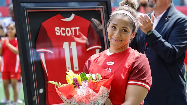 A women's soccer player smiles while holding a bouquet of flowers .