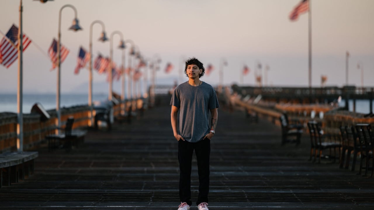 A U.S. veteran stands wistfully on a pier, while American flags billow to his left.