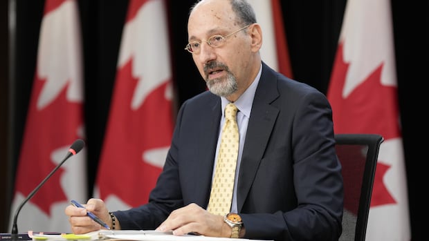 Dr. Zinger is shown sitting at a table with Canadian Flags behind him. 