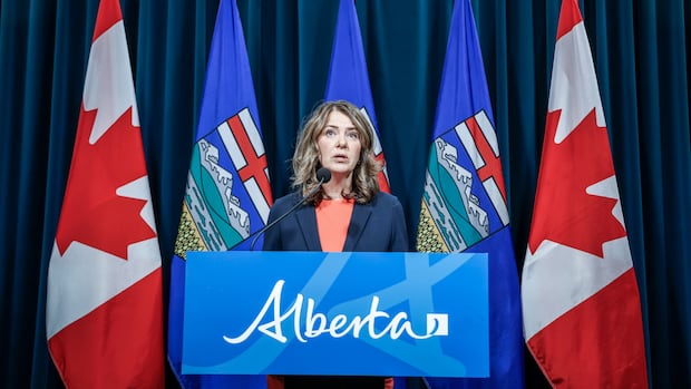 Alberta Premier Danielle Smith provides an update on teacher bargaining in Calgary, on Friday, Oct. 17, 2025. A person stands in front of flags