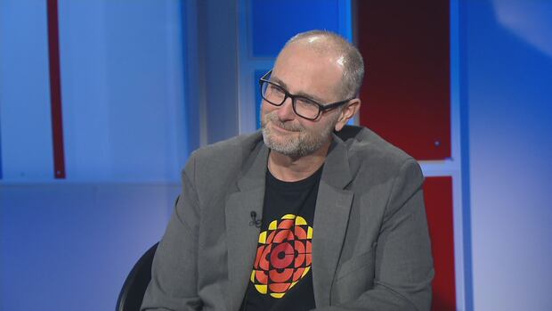 CBC host Matt Rainnie is retiring after more than 30 years at CBC P.E.I. A short haired man in glasses and a CBC shirt sits at a television studio desk.