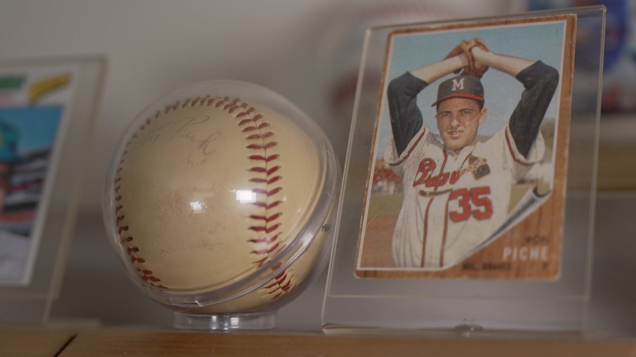 A close-up of a signed and mounted baseball and a faded player's baseball card from the 1960s.