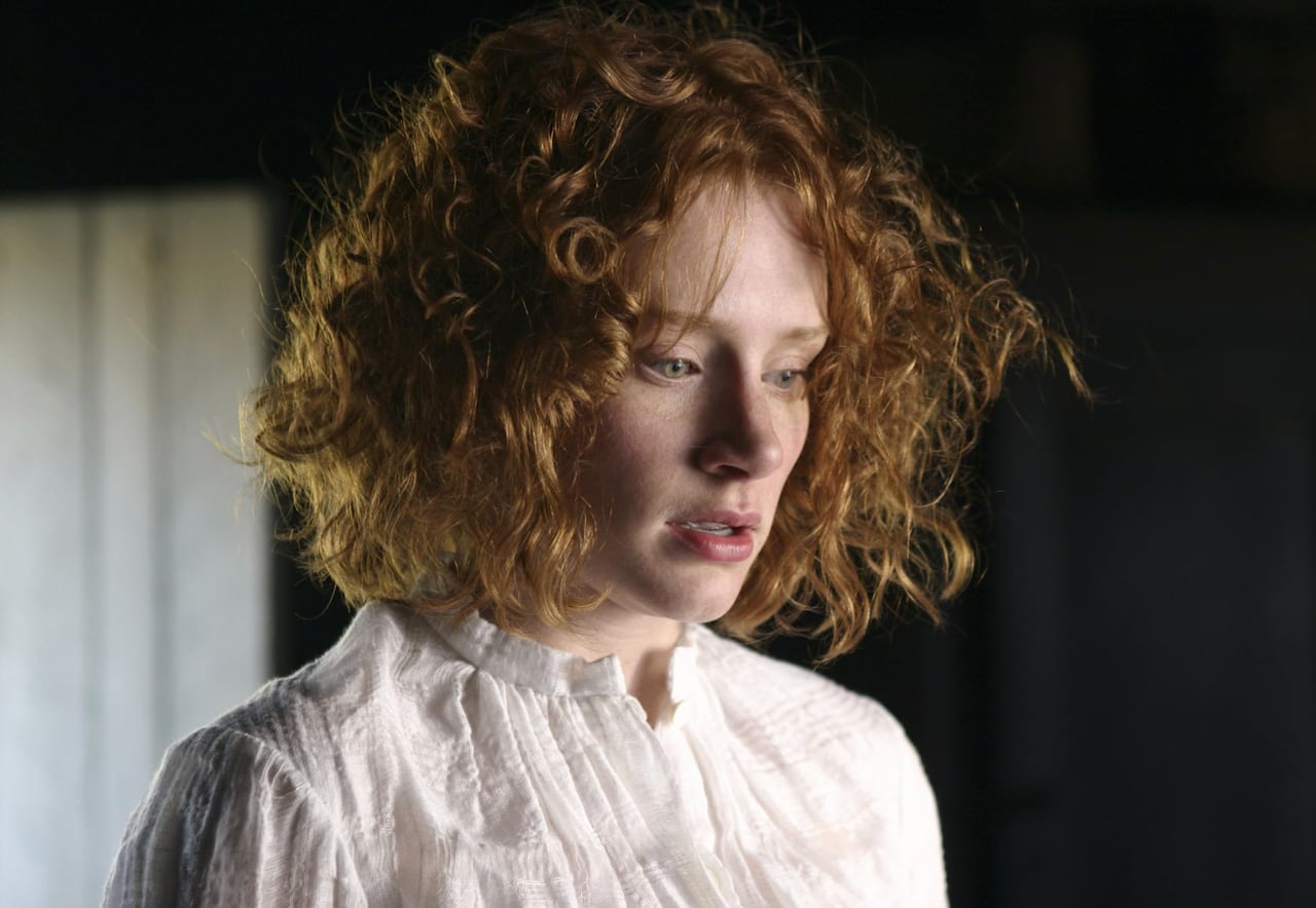 Closeup on a woman with curly hair wearing a white top.