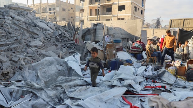 A Palestinian kid walks at the site of an overnight Israeli strike on a house, in Gaza City, October 29, 2025. REUTERS/Ebrahim Hajjaj A small boy is seen in the foreground walking amid concrete debris and tarp in an urban area with damaged buildings. Adults are shown nearby.