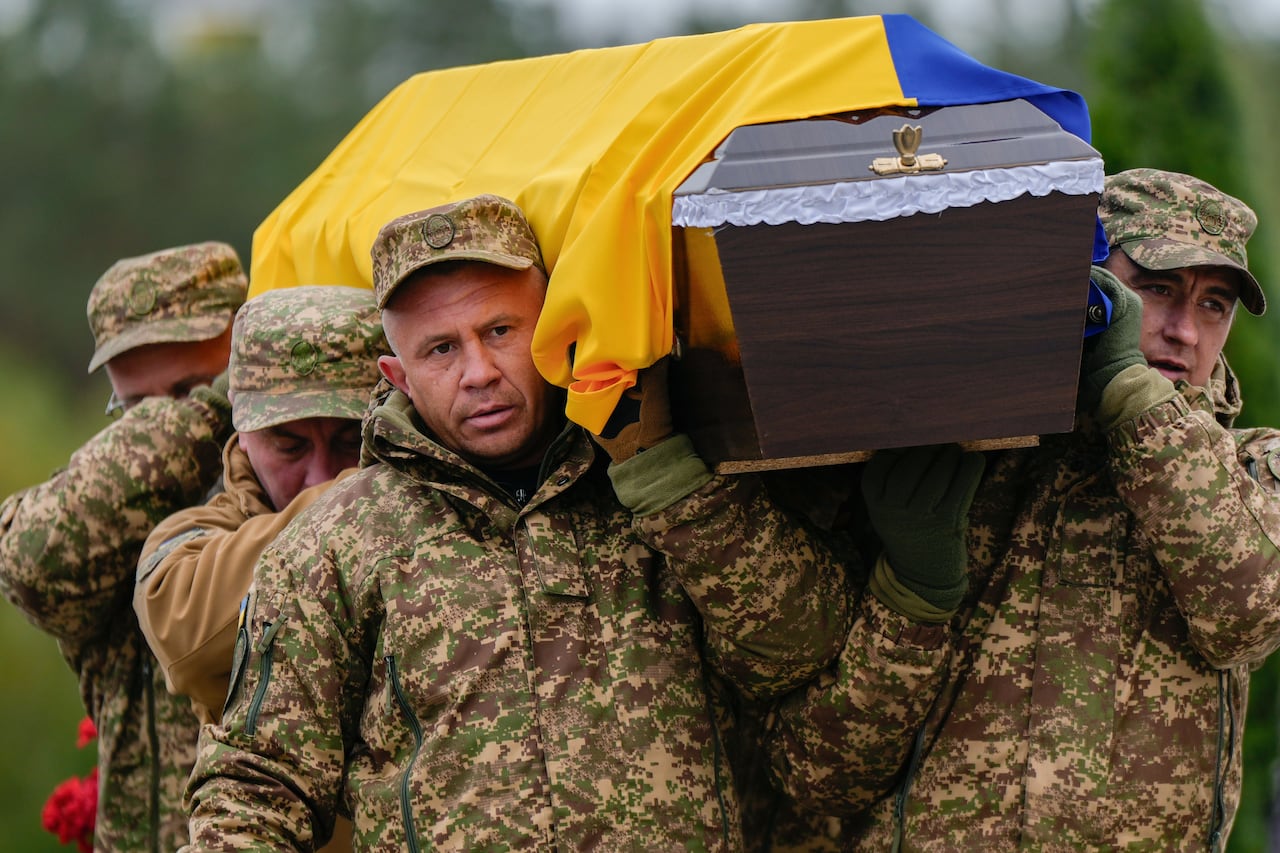 Soldiers wearing fatigues carry a coffin, draped in the Ukrainian flag, on their shoulders. 
