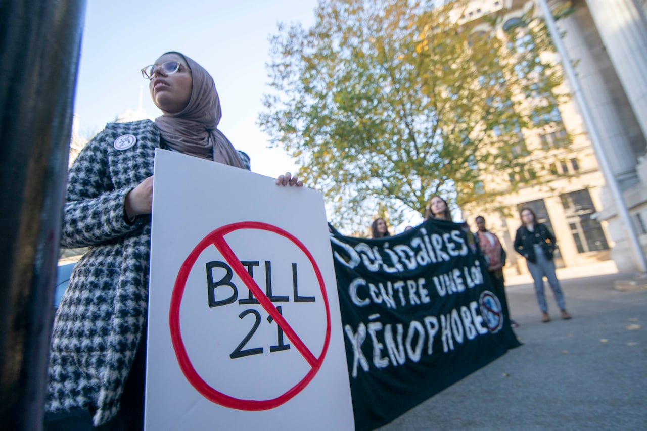 A woman in a hijab holds a sign saying no to bill 21 in front of the Quebec Court of appeal