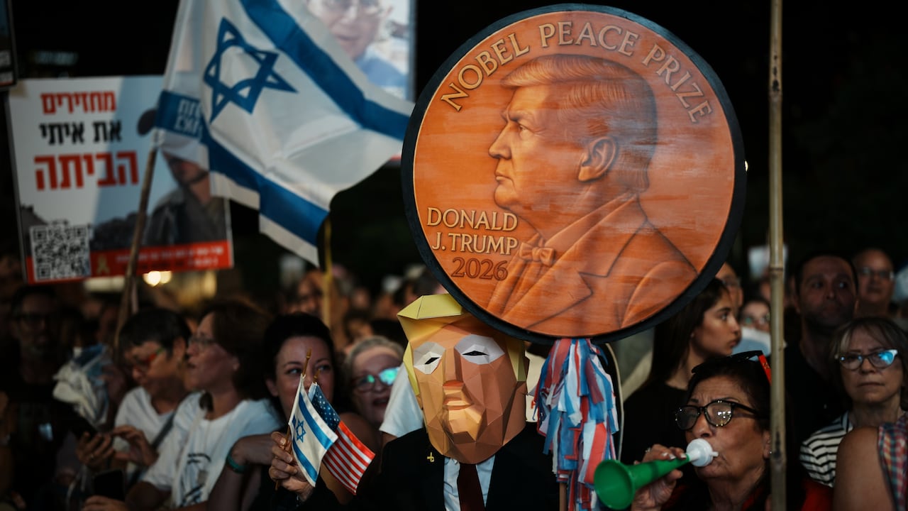 A person wears a mask while holding up a sign depicting a medal.